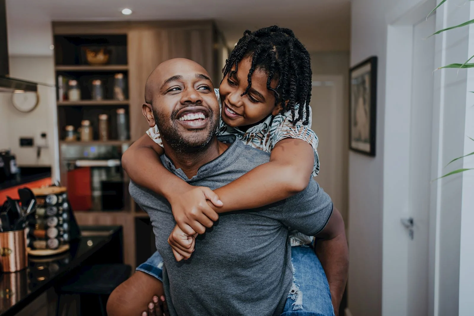 A smiling father carrying his child on his back at home.