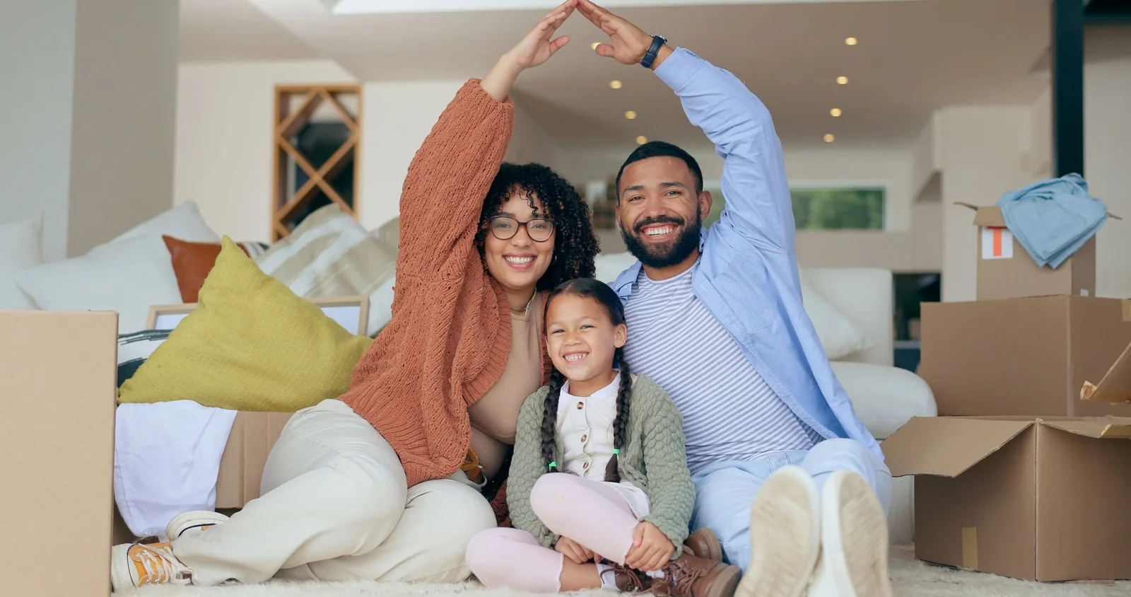 Parents and their child smiling together among moving boxes in their new home.