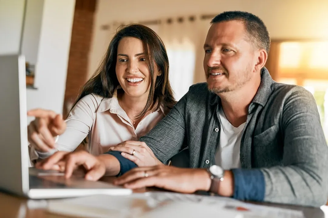 A couple working together at a laptop at home.
