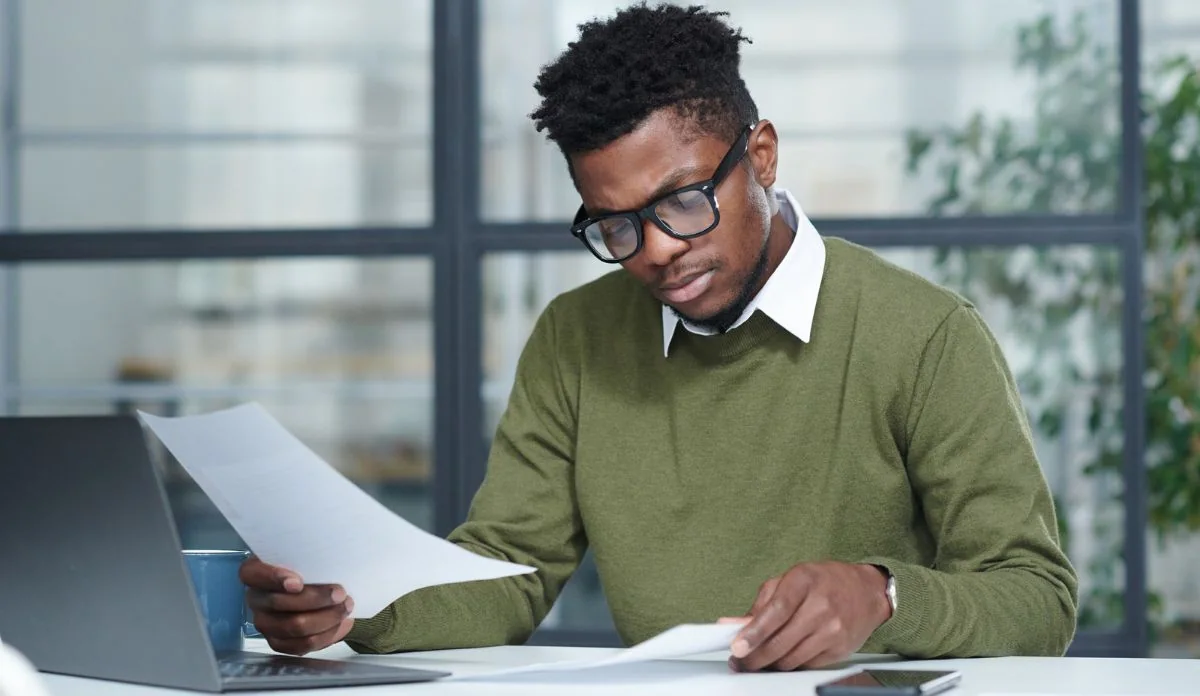 A man reviewing letters and documents beside his laptop.
